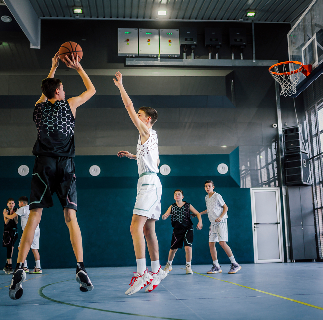 Boys playing basketball indoors, mid-game action.